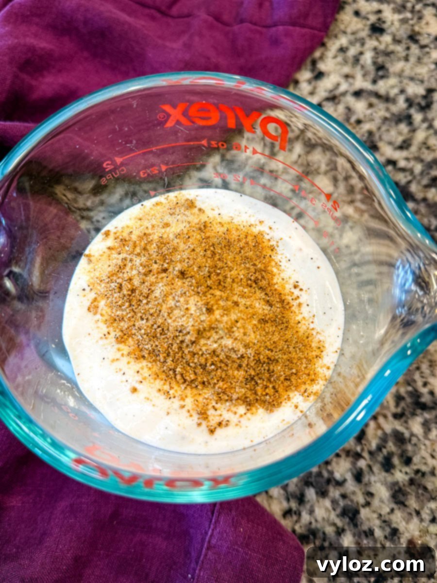A vibrant bowl of creamy ranch dressing, freshly seasoned with a generous sprinkle of aromatic Creole seasoning, ready to be mixed and add its tangy kick to the Southern Cornbread Salad.