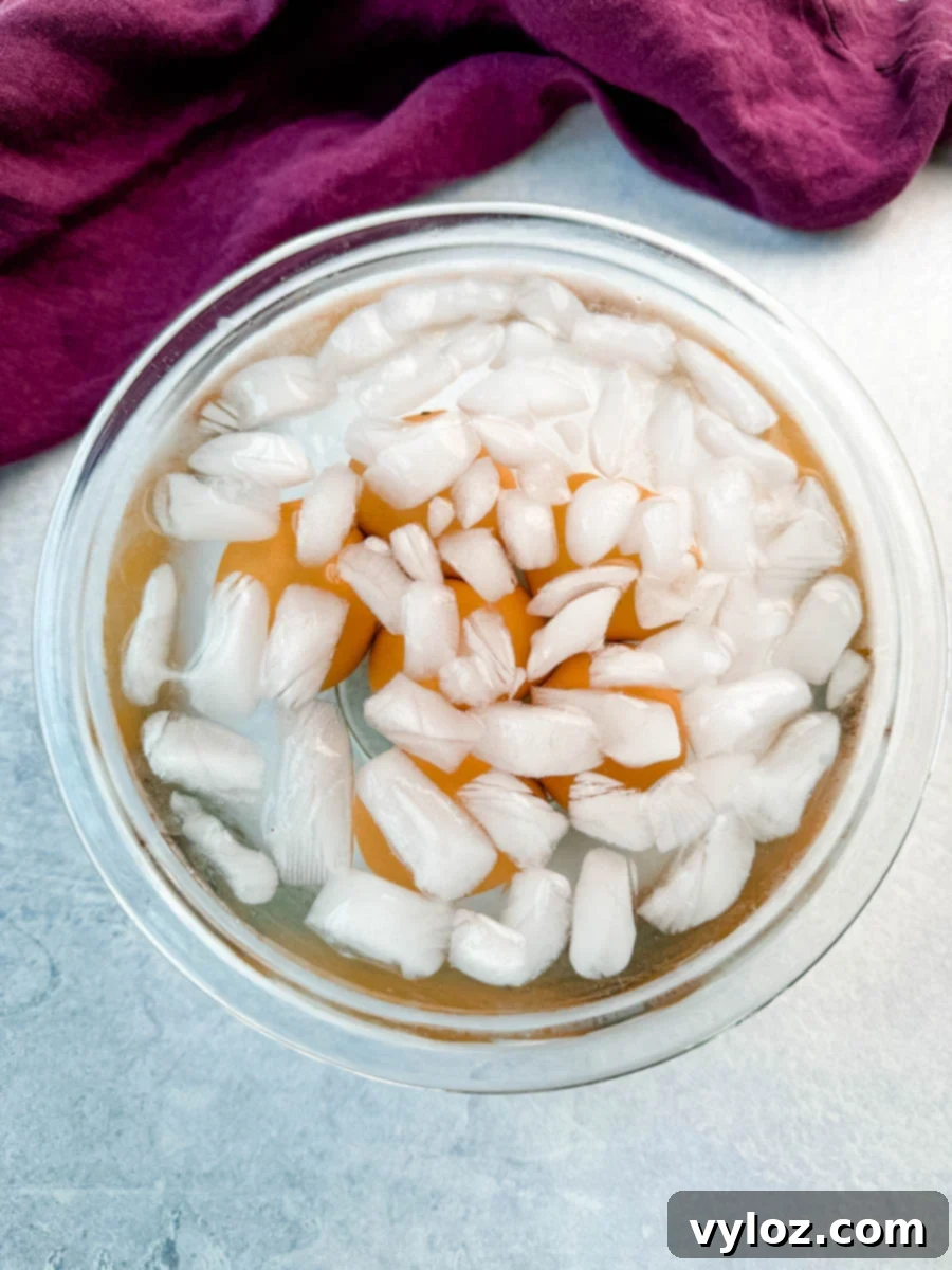 Homestyle Southern Deviled Eggs 7 Brown eggs in a glass bowl filled with ice water after boiling, with a purple cloth in the background.
