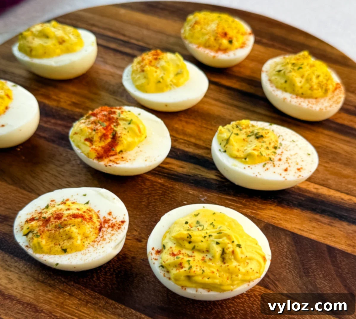 Homestyle Southern Deviled Eggs 10 Overhead view of several deviled eggs arranged on a wooden platter, sprinkled with paprika and herbs.