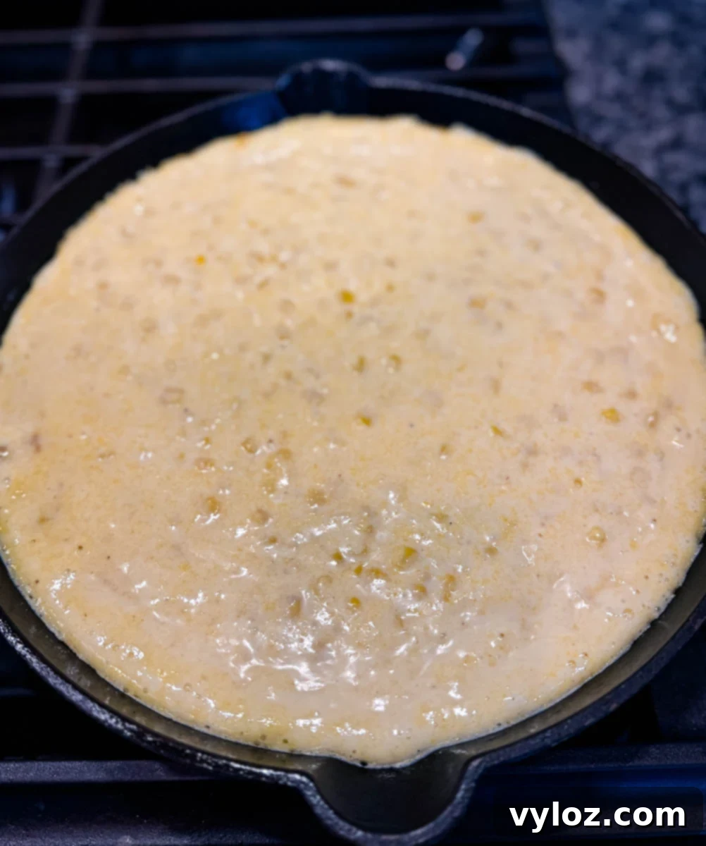 Unbaked Jiffy corn casserole batter in a black cast iron skillet, ready to be baked.