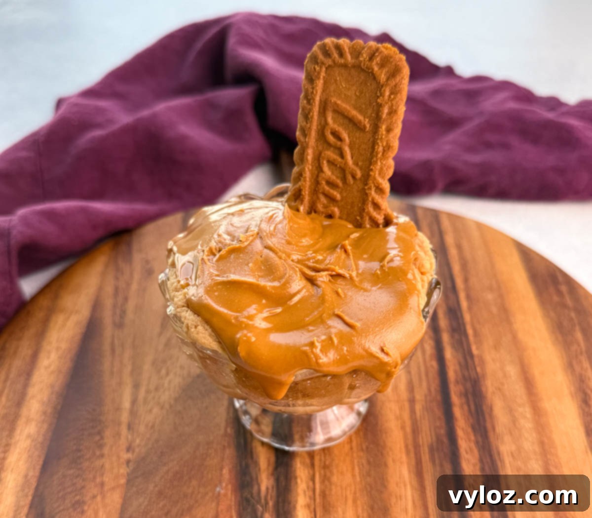 Glass dish of Biscoff protein mug cake topped with a smooth layer of melted Biscoff spread and garnished with a Lotus cookie, purple towel in background.