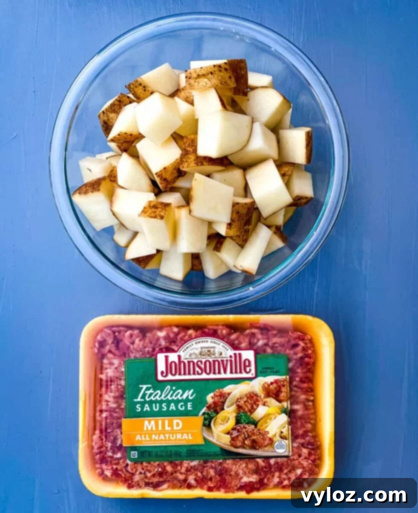 Chopped russet potatoes in a glass bowl next to a package of Italian sausage, ready for cooking