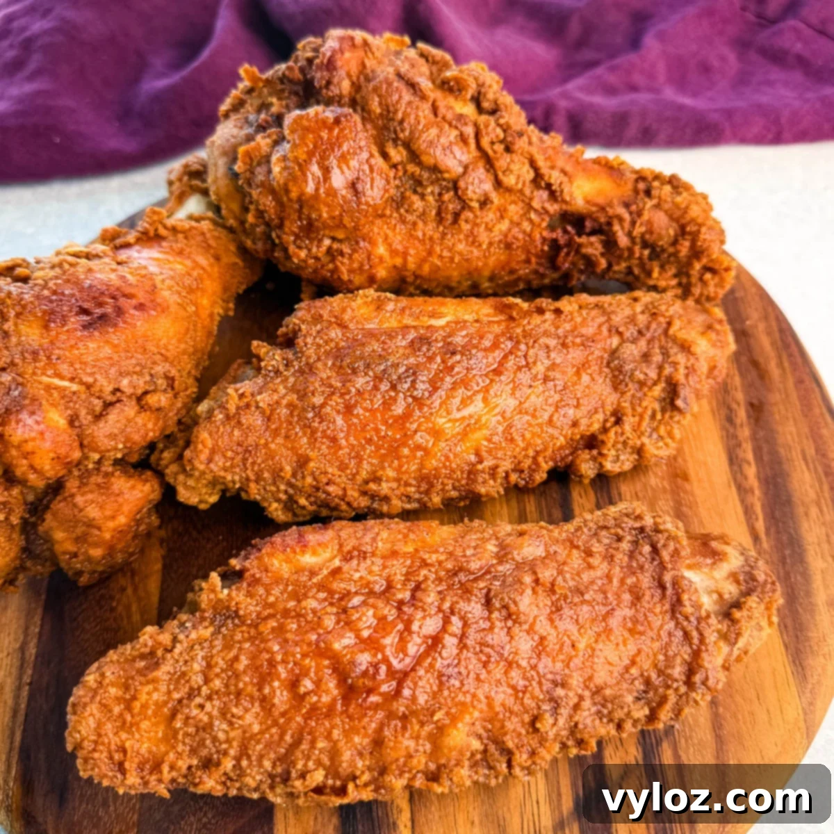Close-up of golden brown fried turkey wings stacked on a round wooden board, with a deep purple cloth in the background.