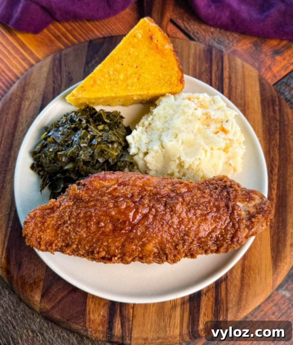 Overhead view of a plate with a fried turkey wing, collard greens, mashed potatoes, and a triangular slice of cornbread, served on a wooden board.