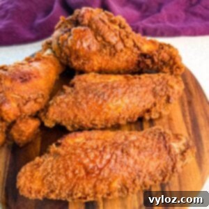 Close-up of golden brown fried turkey wings stacked on a round wooden board, with a deep purple cloth in the background.