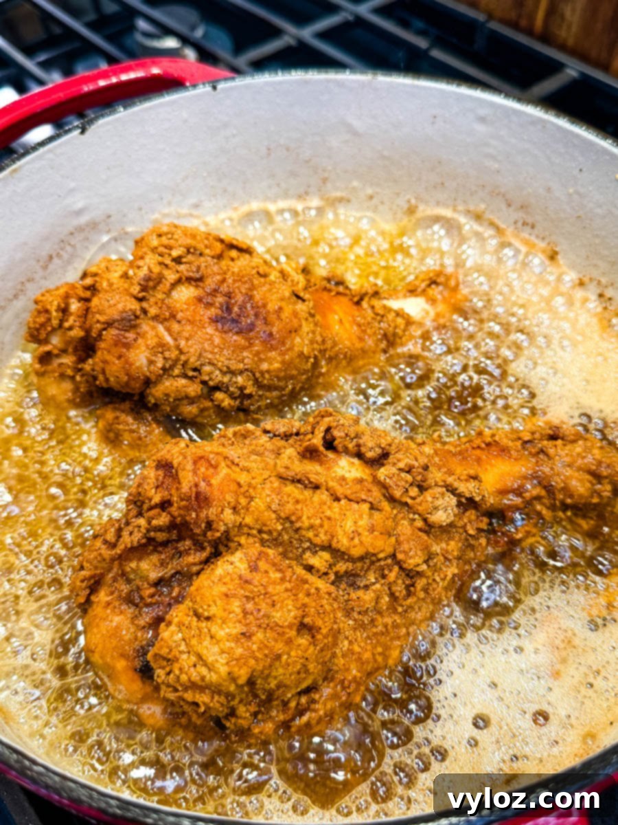 Turkey wings frying in hot oil in a red Dutch oven, with bubbling oil surrounding the wings.