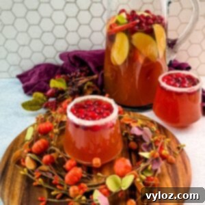 Golden Harvest Punch 10 Pitcher of Thanksgiving punch with apple slices and cranberries, served with two sugared-rim glasses of punch on a round wooden board.