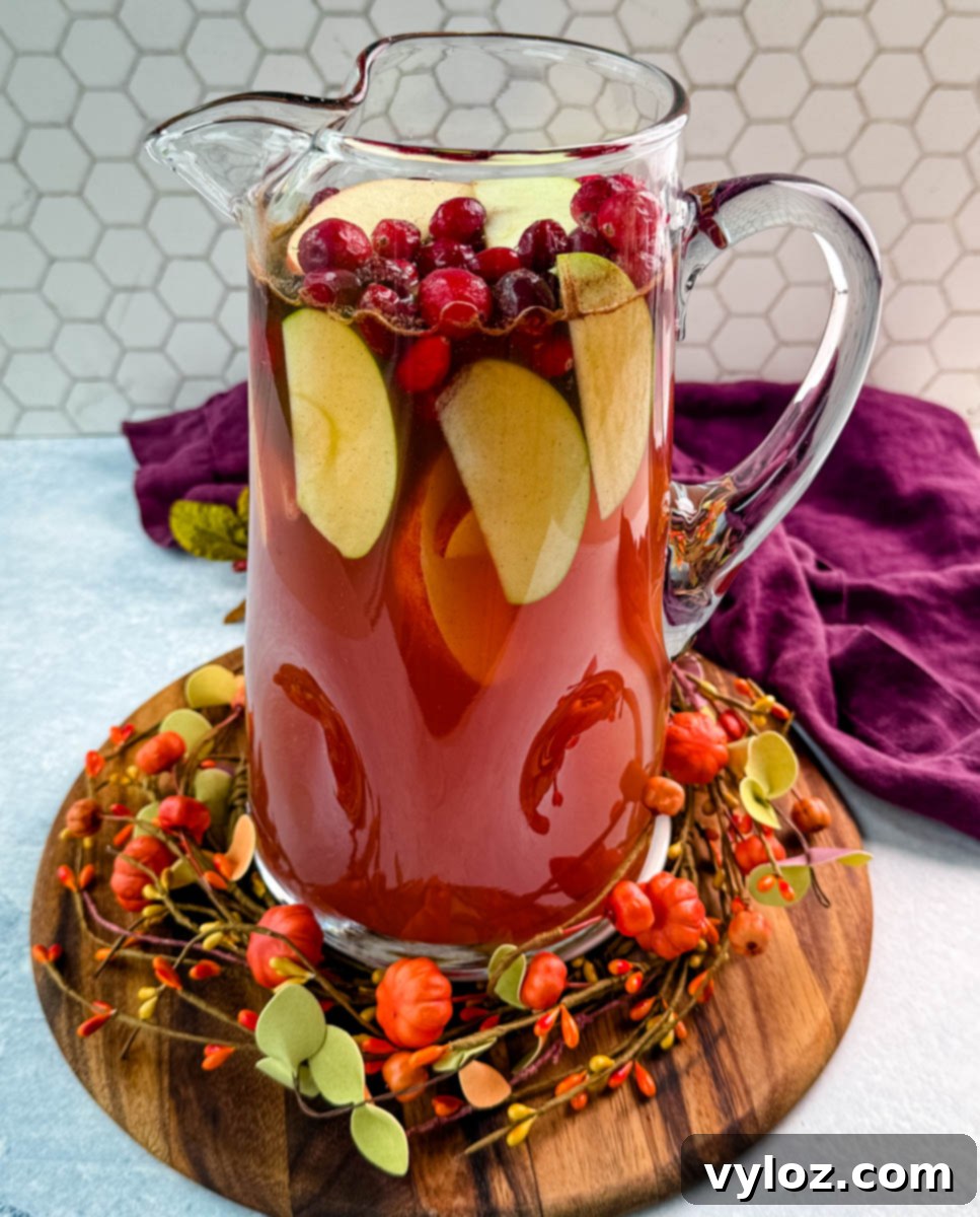 Golden Harvest Punch 7 Tall pitcher of Thanksgiving punch filled with apple slices and cranberries, sitting on a fall wreath centerpiece.