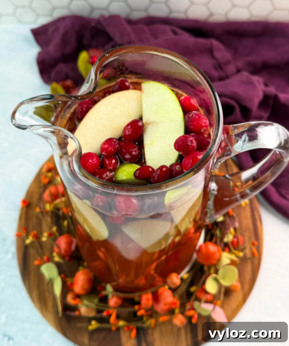 Golden Harvest Punch 8 Overhead view of a pitcher of Thanksgiving punch filled with green apple slices and fresh cranberries, surrounded by autumn décor.