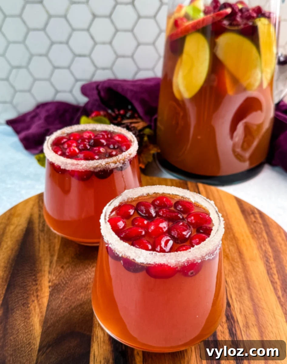 Golden Harvest Punch 9 Two glasses of Thanksgiving punch with sugared rims and cranberries in front of a pitcher of punch filled with apples and cranberries.