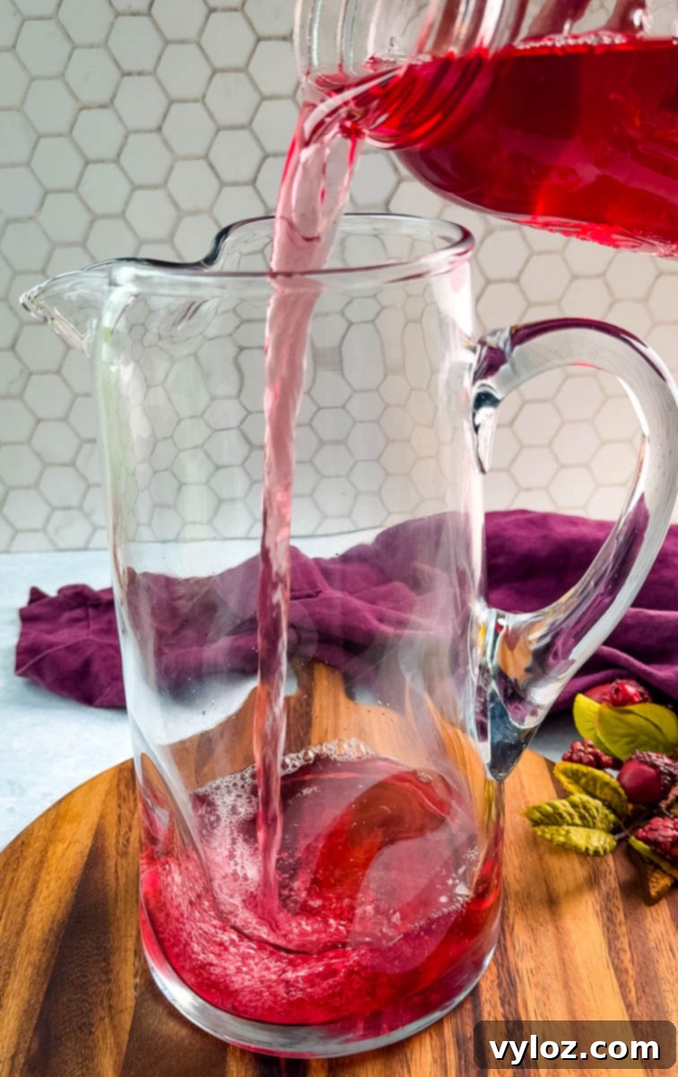 Yuletide Cheer Punch 5 Rich cranberry juice gracefully cascading into a clear pitcher, forming the vibrant red base for the Christmas punch.