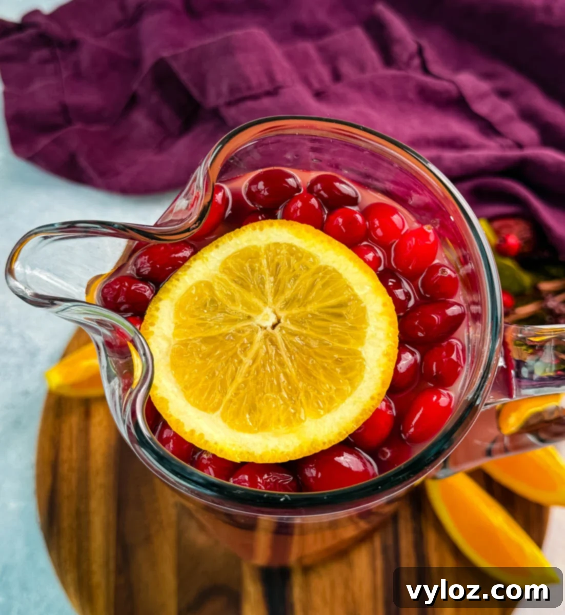 Yuletide Cheer Punch 9 A close-up, top-down view of a glass pitcher brimming with festive punch, showcasing the beautiful floating fresh cranberries and a prominent slice of orange on the surface, ready to be served.