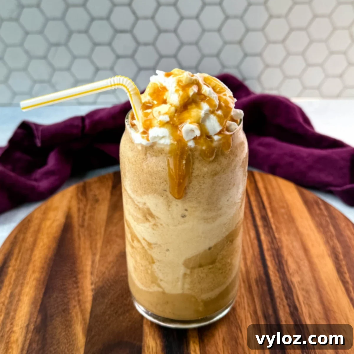 A tall, elegant glass of homemade pumpkin spice frappé, generously topped with fluffy whipped cream and a luxurious caramel drizzle. A straw invites you to take the first sip of this autumnal delight.