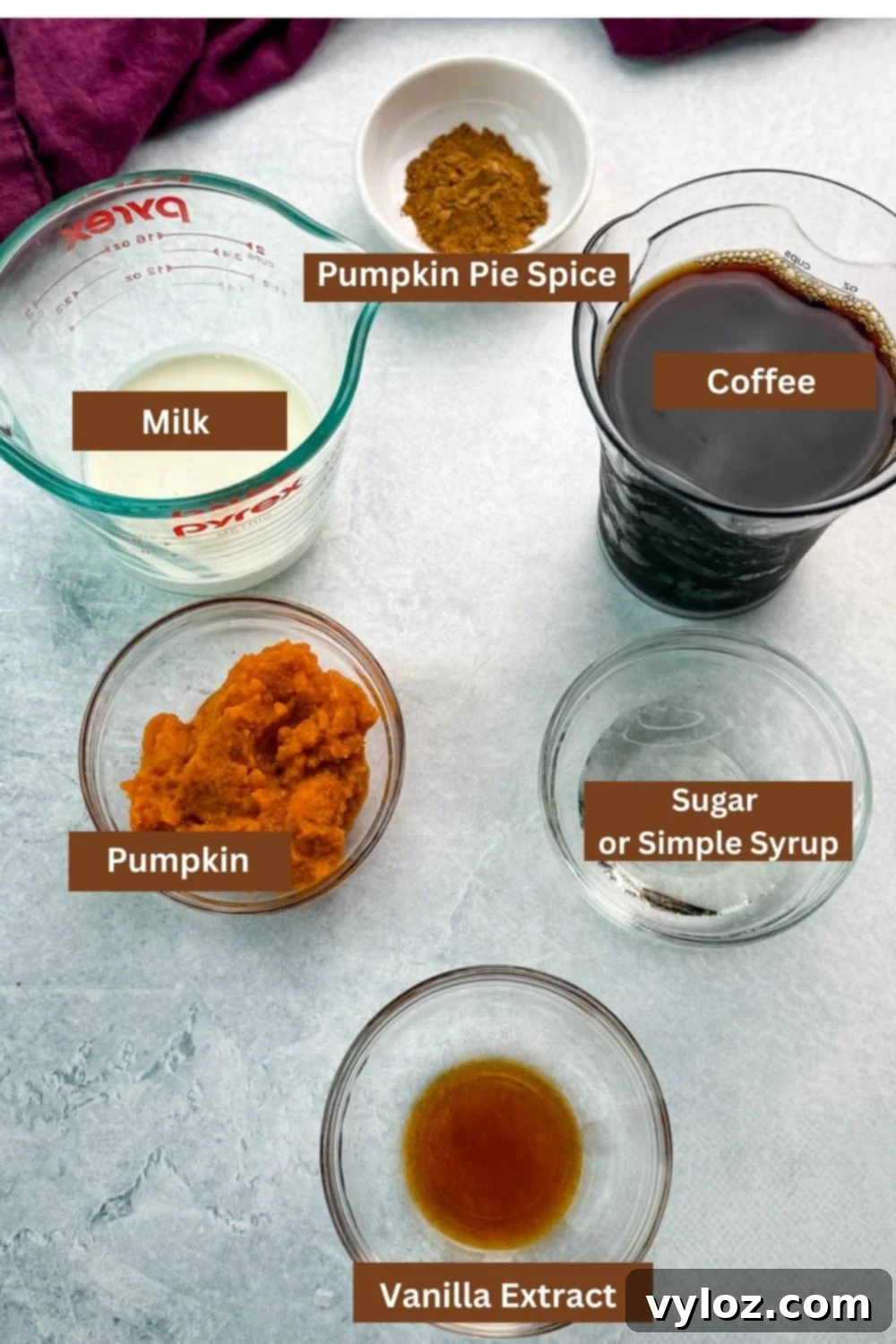 Glass bowls and measuring cups neatly arranged on a countertop, filled with fresh ingredients for a pumpkin spice frappé: rich milk, strong brewed coffee, smooth pumpkin purée, fragrant vanilla extract, granulated sugar or clear simple syrup, and a generous heap of aromatic pumpkin pie spice.