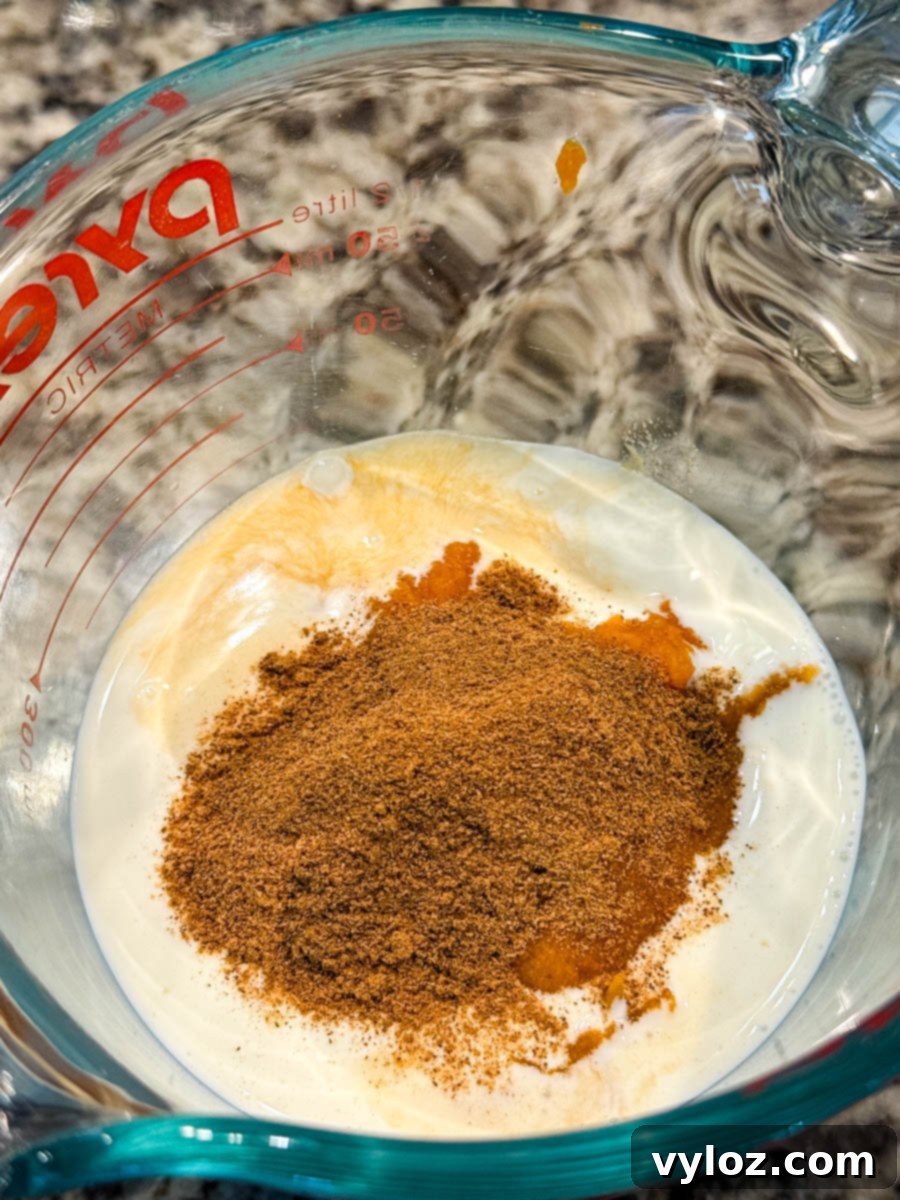 A glass measuring cup holds a creamy mixture of milk, smooth pumpkin purée, fragrant vanilla extract, and rich pumpkin pie spice, ready to be combined with coffee for the ultimate frappé.