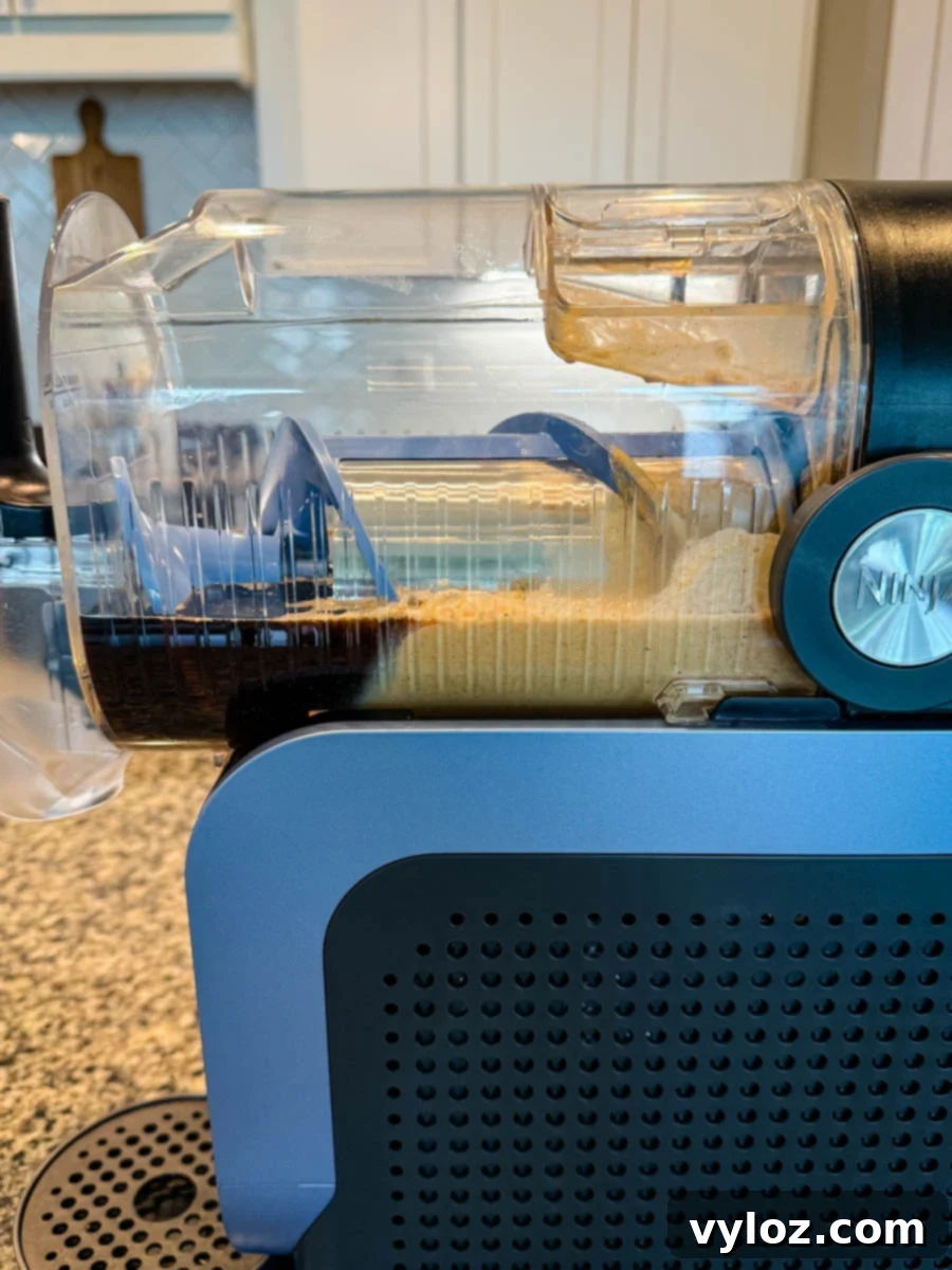 The delicious coffee and pumpkin spice mixture is seen swirling and transforming inside the clear container of a Ninja Slushi machine, beginning its journey to becoming a perfect frozen frappé.