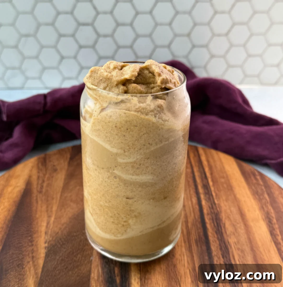 A tall, clear glass filled with a perfectly thick and textured pumpkin spice frappé, ready to be enjoyed. The swirls indicate its creamy consistency.