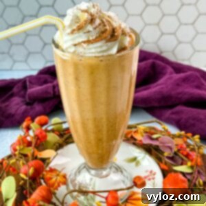 Ninja Slushi's Autumn Spice Elixir 9 A tall glass filled with pumpkin spice milkshake topped with whipped cream and sprinkled with cinnamon, sitting on a fall-themed wooden tray decorated with small pumpkins and leaves.