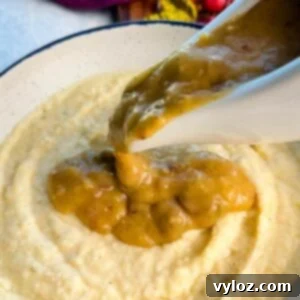 Golden turkey giblet gravy being poured generously from a white gravy boat over a bowl of creamy grits.