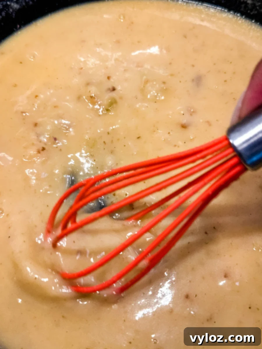 Giblet gravy being whisked smooth in a skillet with a bright red whisk.