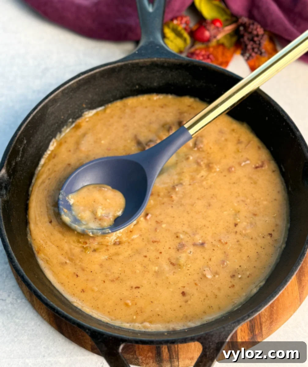 Top view of a skillet of smooth and chunky turkey giblet gravy, with a blue spoon resting inside.