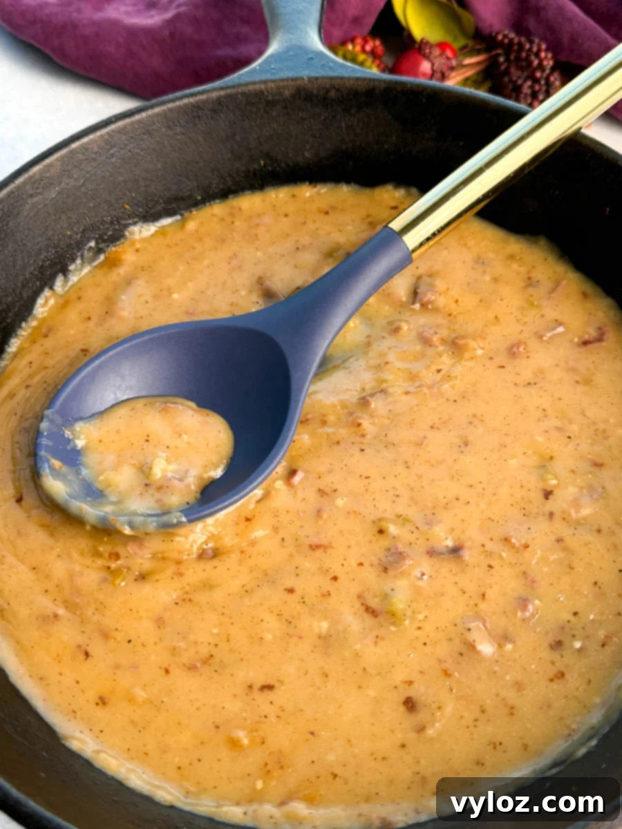 Cast iron skillet filled with thick turkey giblet gravy, with a blue and gold spoon lifting a scoop of the chunky, seasoned gravy.