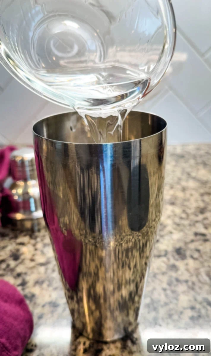 Close-up of vodka being poured into a stainless steel cocktail shaker.