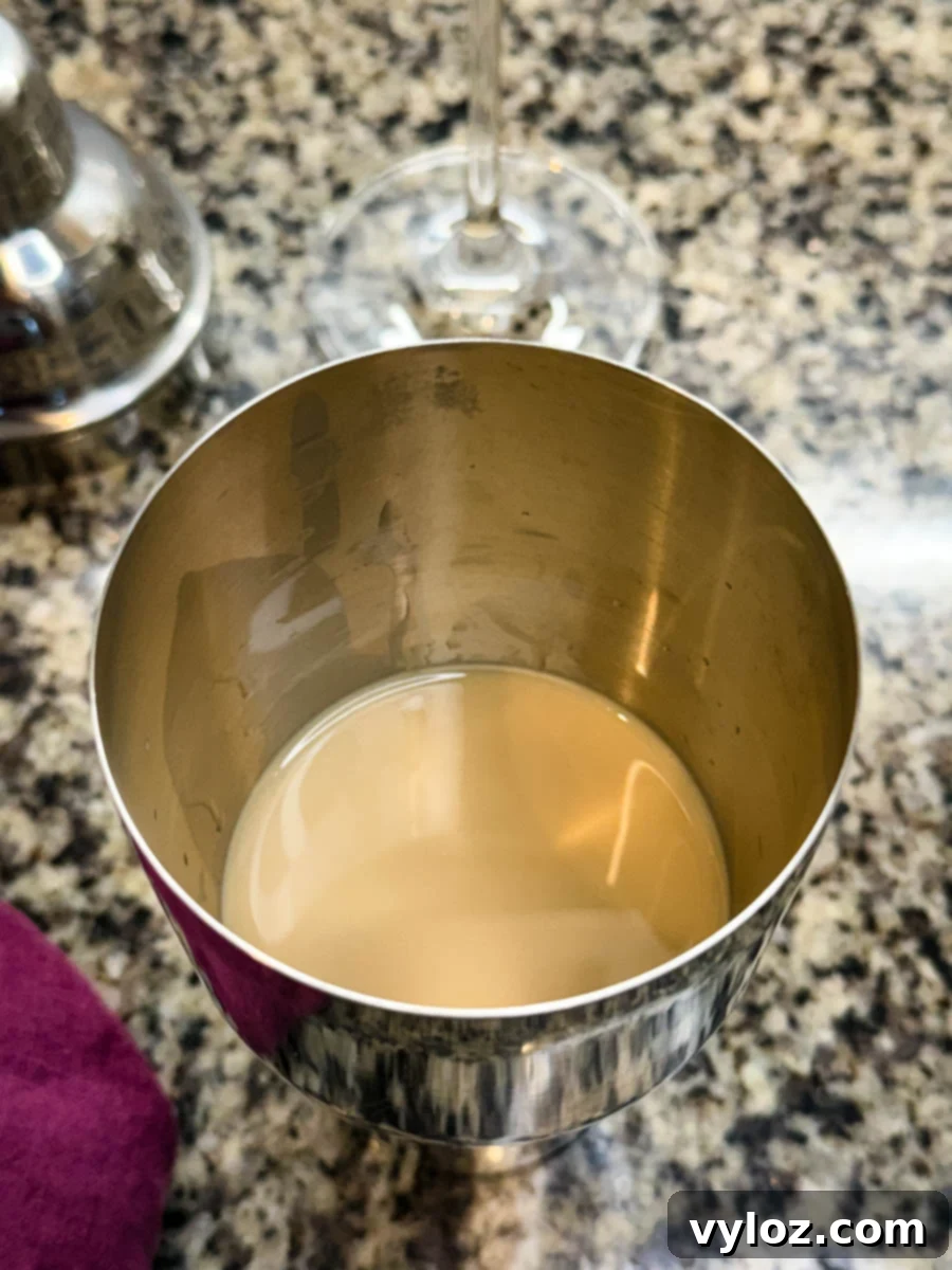 A cocktail shaker containing a smooth, light brown espresso martini mixture before shaking.