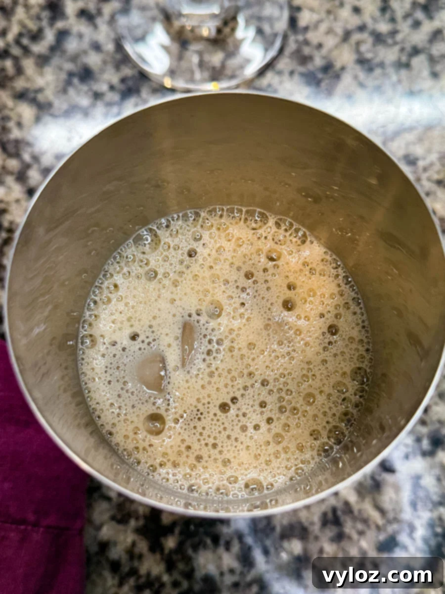 A cocktail shaker filled with a frothy espresso martini mixture over ice, showing bubbles forming on top.