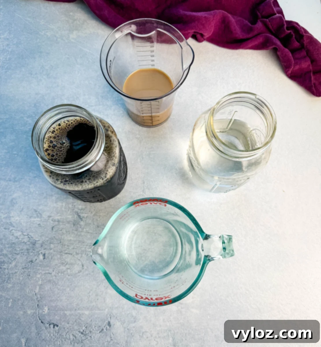 Frozen Shadow Espresso Martini 3 Overhead of ingredients in jars and measuring cups: vodka, coffee liqueur or Irish cream, espresso or cold brew, and water, with a purple cloth in the background. Image 9: Styled shot of two sugar-rimmed glasses filled with espresso martini slush on a wooden board, topped with coffee beans.