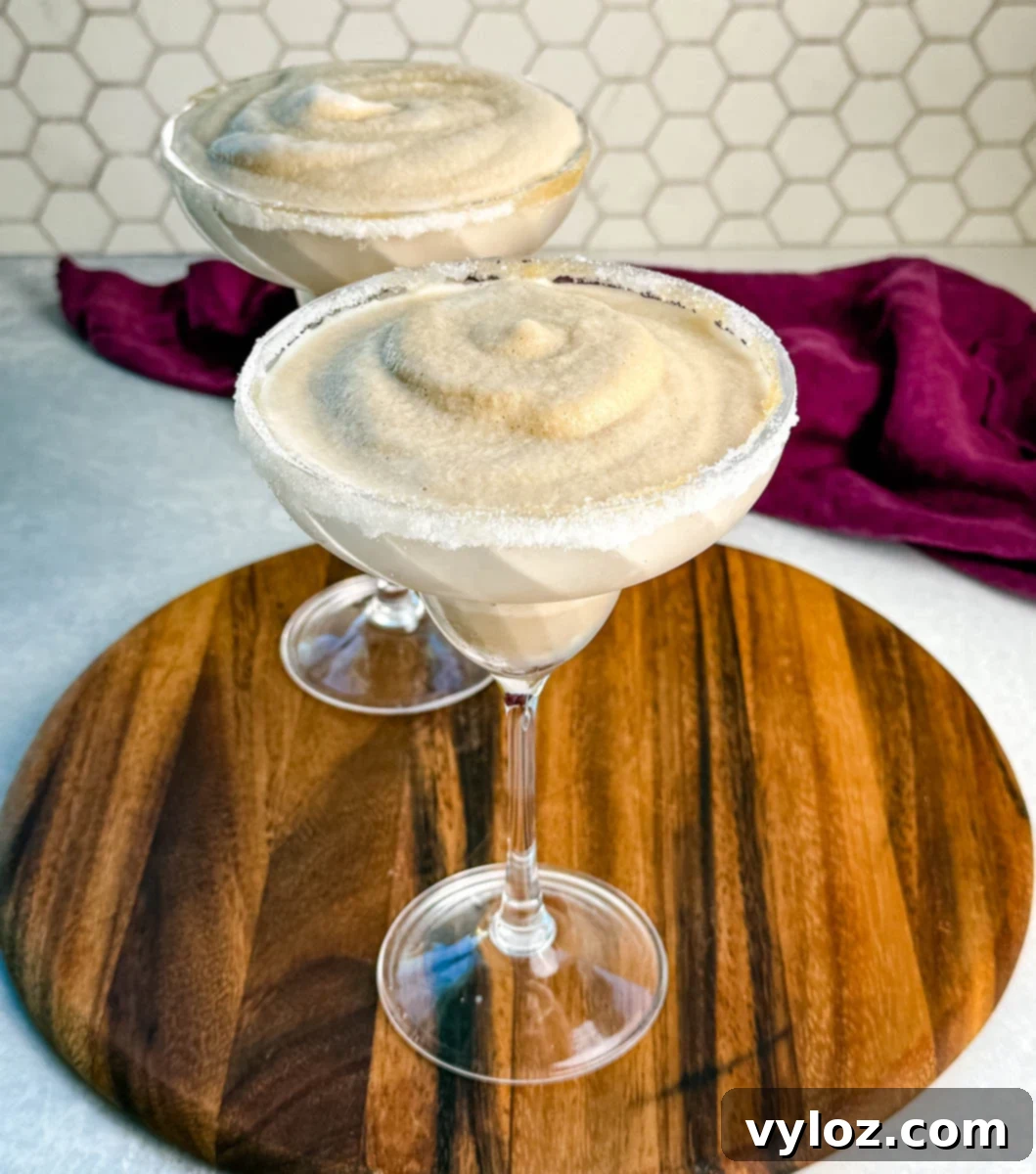 Frozen Shadow Espresso Martini 8 Two espresso martinis with icy, creamy texture in sugar-rimmed glasses, displayed on a round wooden board.