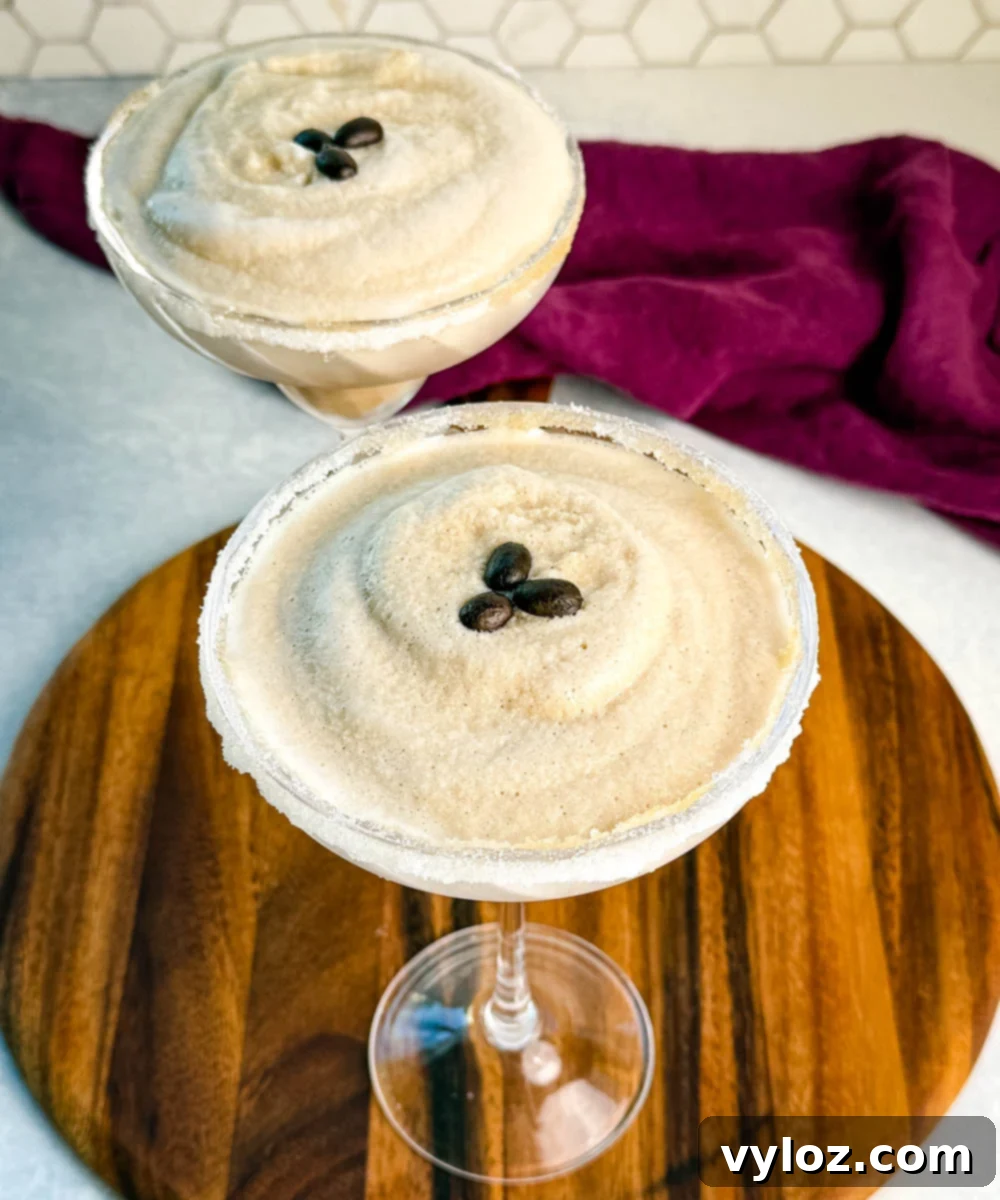 Frozen Shadow Espresso Martini 9 Two frozen espresso martinis in sugar-rimmed glasses topped with coffee beans, served on a wooden board with a purple cloth in the background.