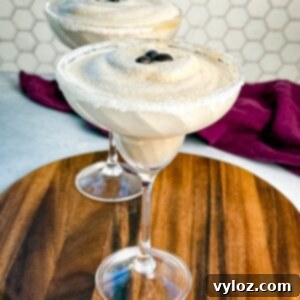 Frozen Shadow Espresso Martini 10 Two frozen espresso martinis in sugar-rimmed glasses topped with coffee beans, served on a wooden board with a purple cloth in the background.