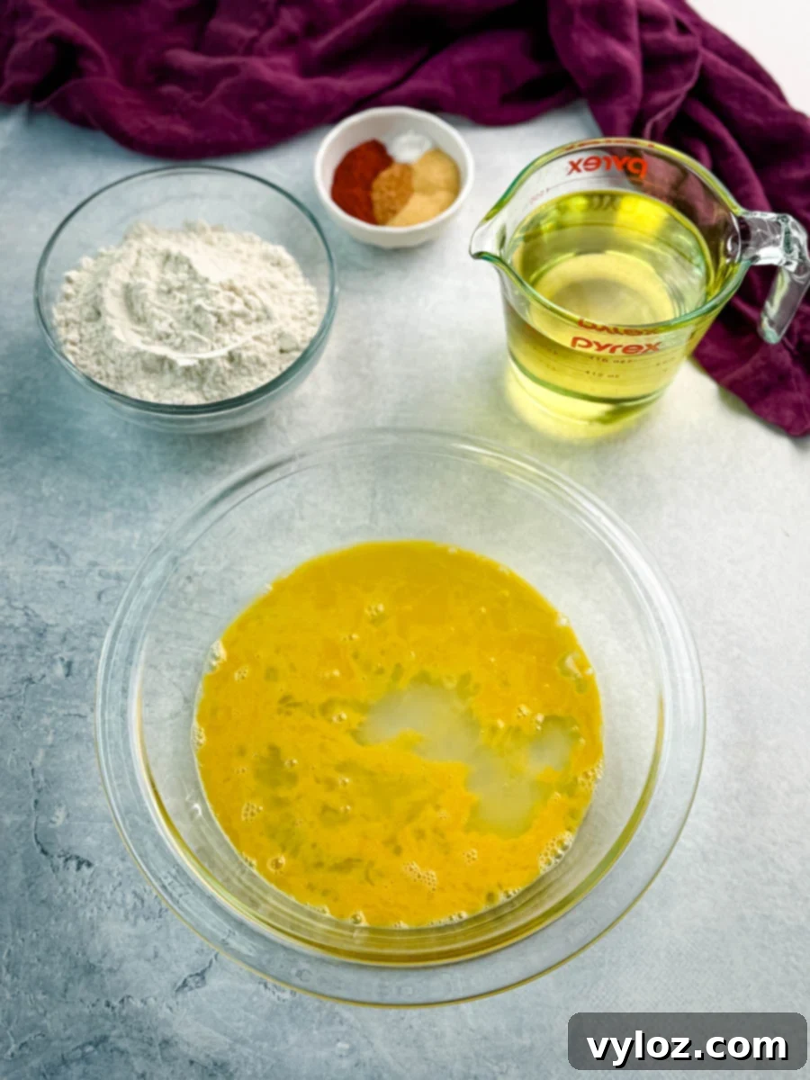 Ingredients laid out for frying gizzards, including a bowl of seasoned flour, a measuring cup of oil, a bowl of beaten egg wash, and a small dish of spices.
