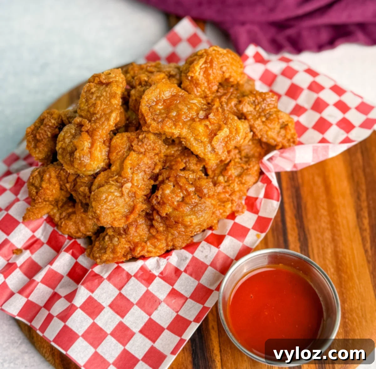 Basket of fried chicken gizzards on red and white checkered paper, served with a small cup of red dipping sauce.
