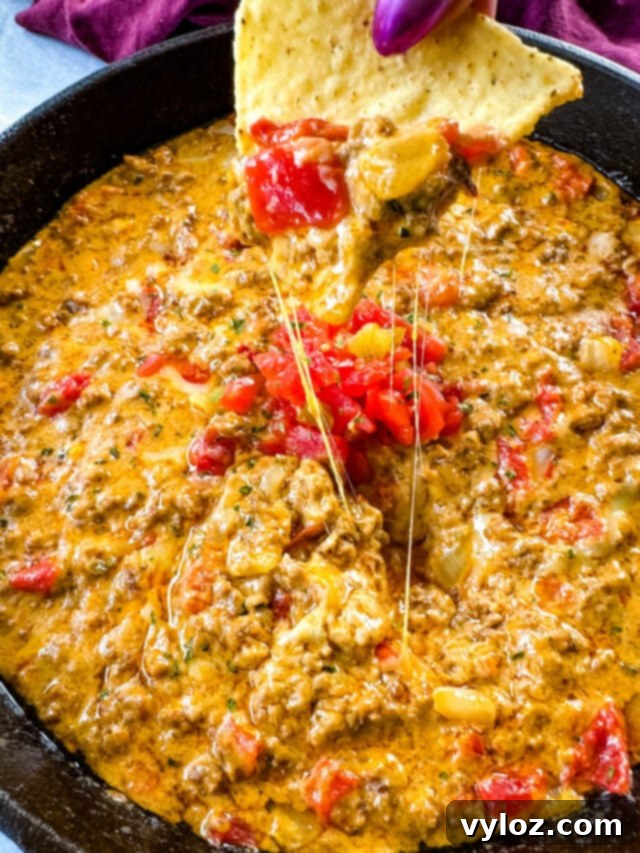 person holding chip with Rotel cheese dip with ground beef in a skillet