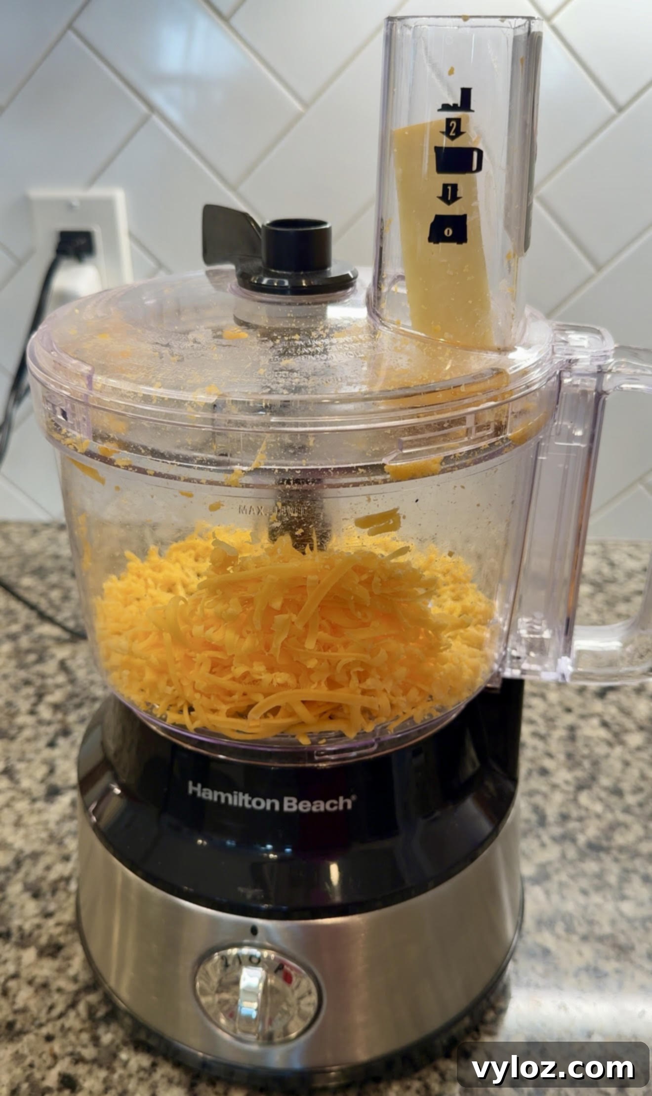 Soulful Golden Baked Macaroni and Cheese 6 Food processor with a block of cheddar cheese in the chute, ready to be shredded.