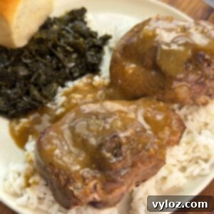 Plate of turkey chops smothered in brown gravy over rice, served with collard greens and a dinner roll.
