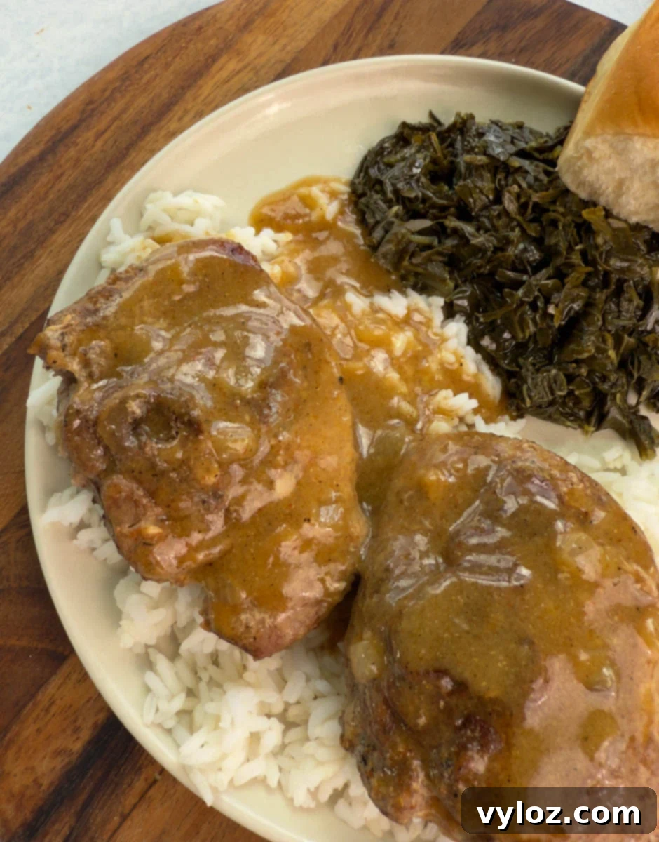 Close-up of smothered turkey chops with brown gravy served over rice, collard greens, and a roll.