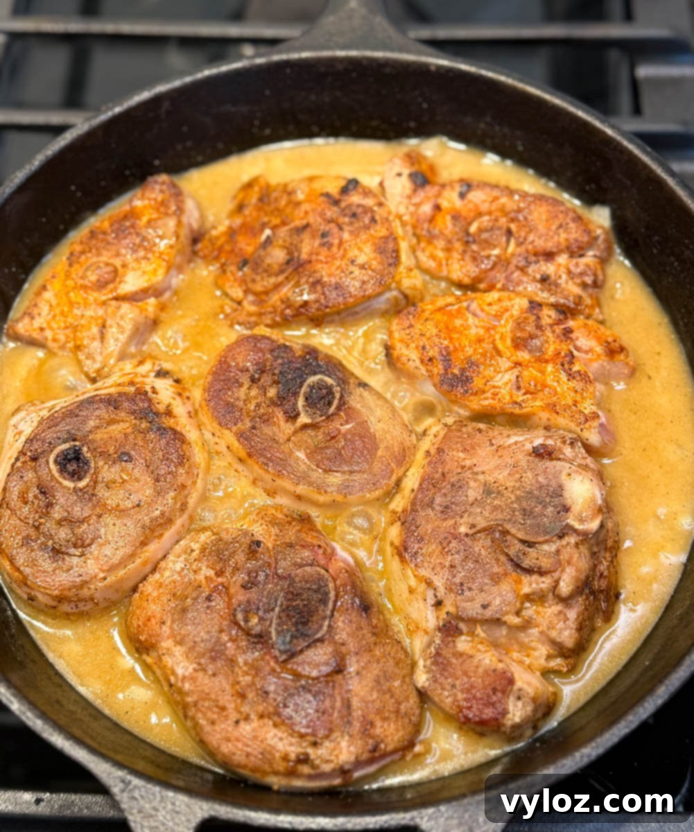 Cast iron skillet filled with browned turkey chops simmering in rich golden gravy.