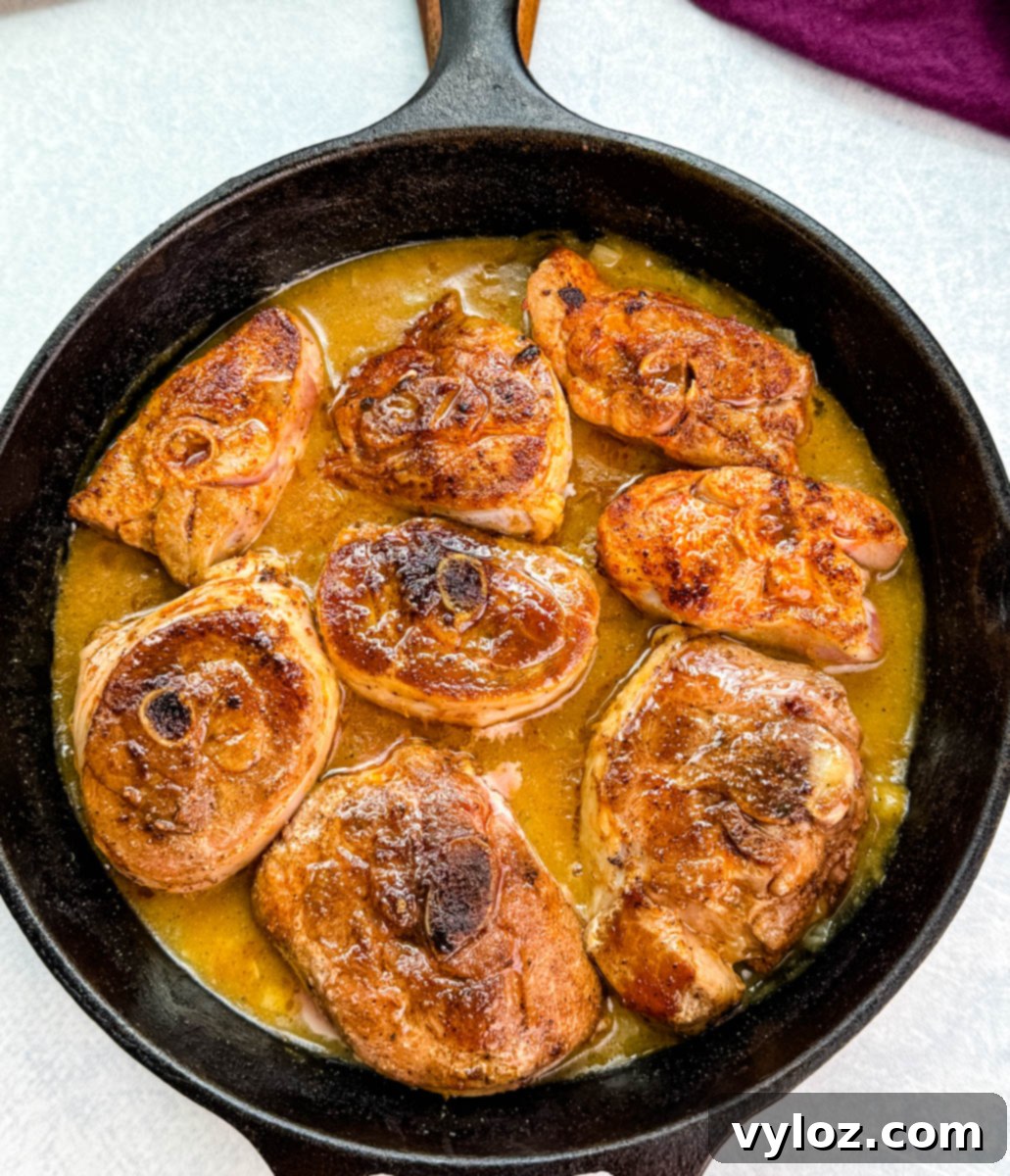 Overhead view of turkey chops in gravy, glistening in a cast iron skillet on a light background.