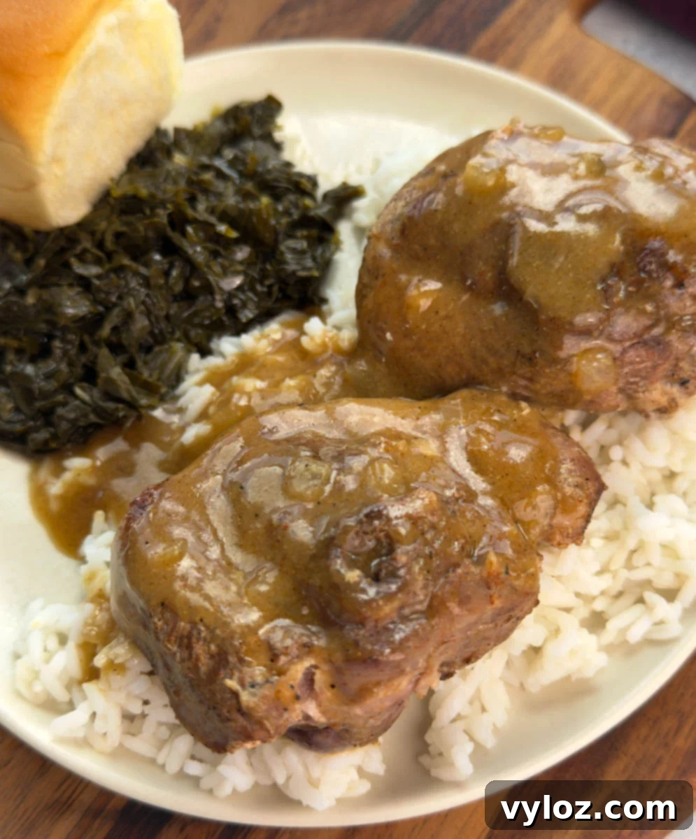 Plate of turkey chops smothered in brown gravy over rice, served with collard greens and a dinner roll.