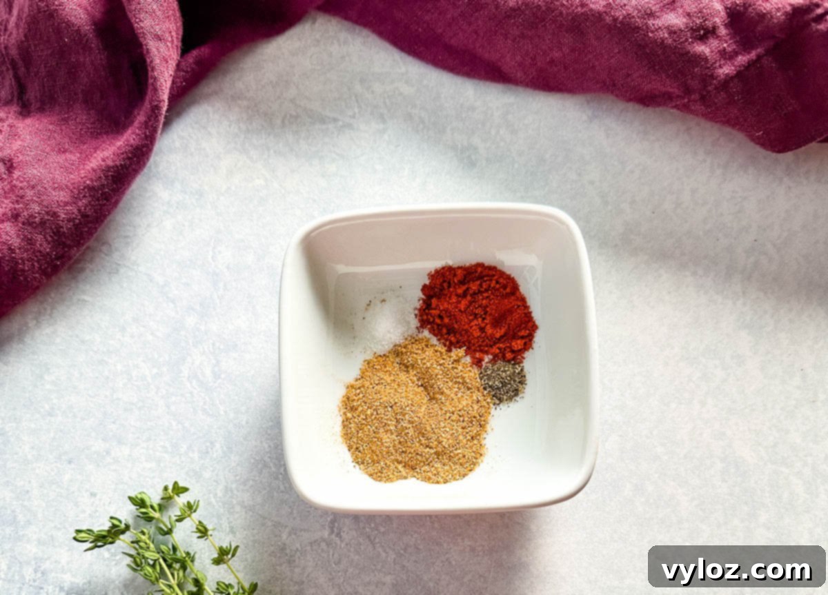 A small white dish filled with a spice blend, including paprika, black pepper, and garlic powder, with a sprig of fresh thyme nearby on the counter.