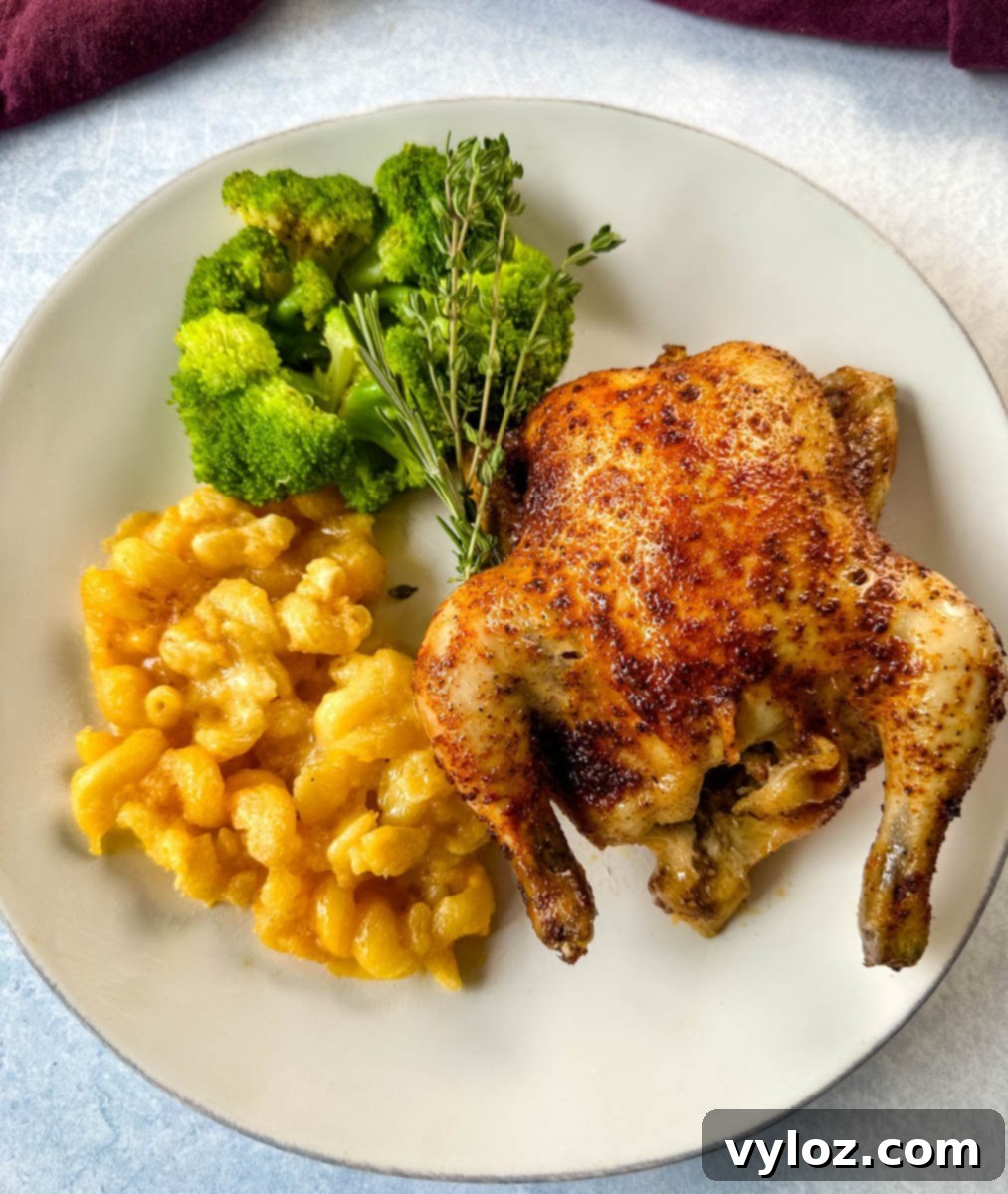 A plated serving with one baked Cornish hen alongside bright green broccoli florets and creamy baked macaroni and cheese, garnished with fresh thyme.