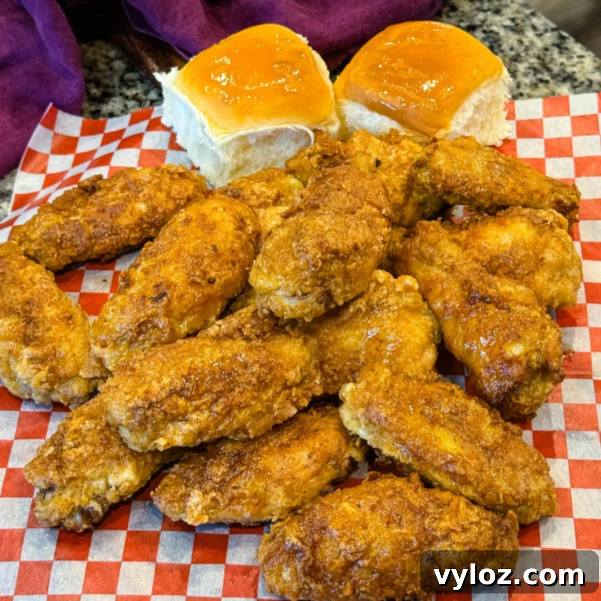 Overhead shot of crispy fried chicken wings on checkered paper, served with dinner rolls, fries, ranch, and buffalo dipping sauce.