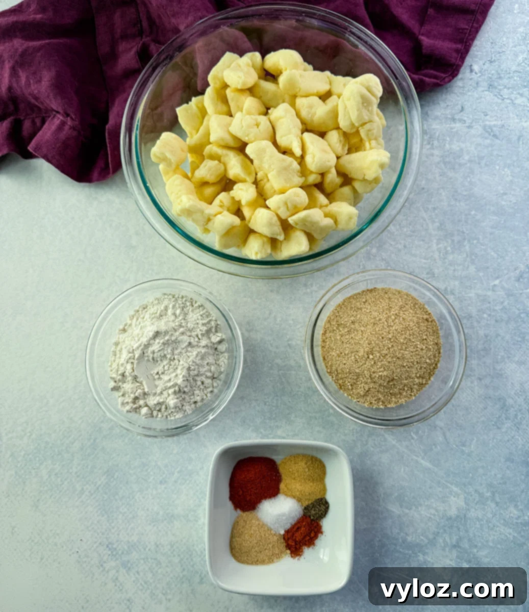 Overhead view of cheese curd ingredients in bowls: fresh cheese curds, flour, breadcrumbs, and a mix of colorful spices on a light background.