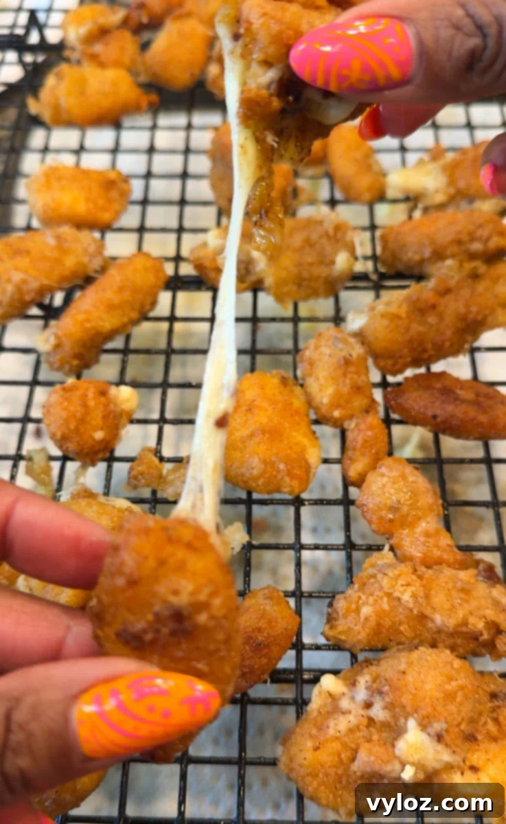 Close-up of golden fried cheese curds on a cooling rack with gooey melted cheese stretching between two pieces being pulled apart by hand.
