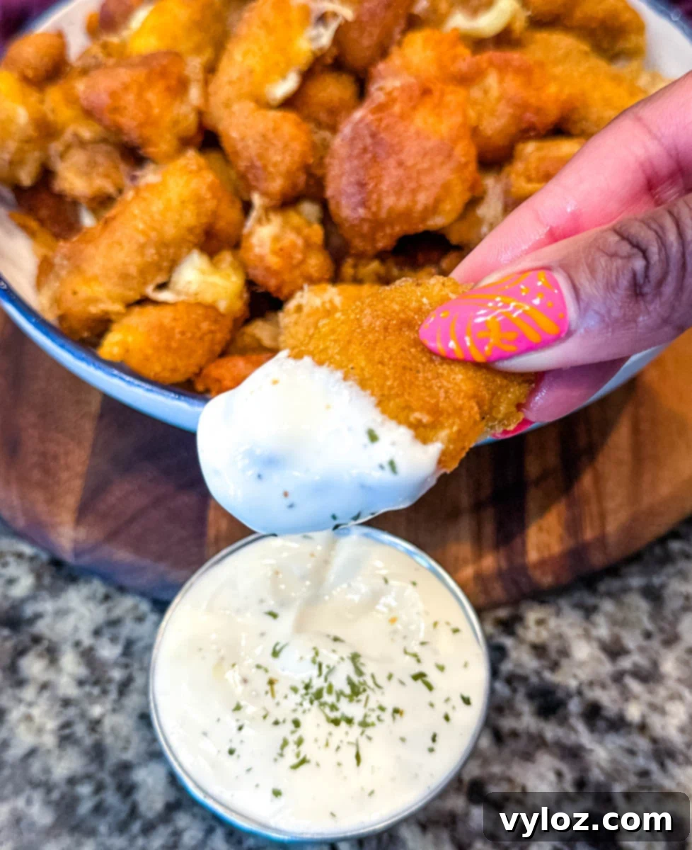 Fried cheese curd being dipped into ranch dressing, with a large bowl of golden brown curds in the background.