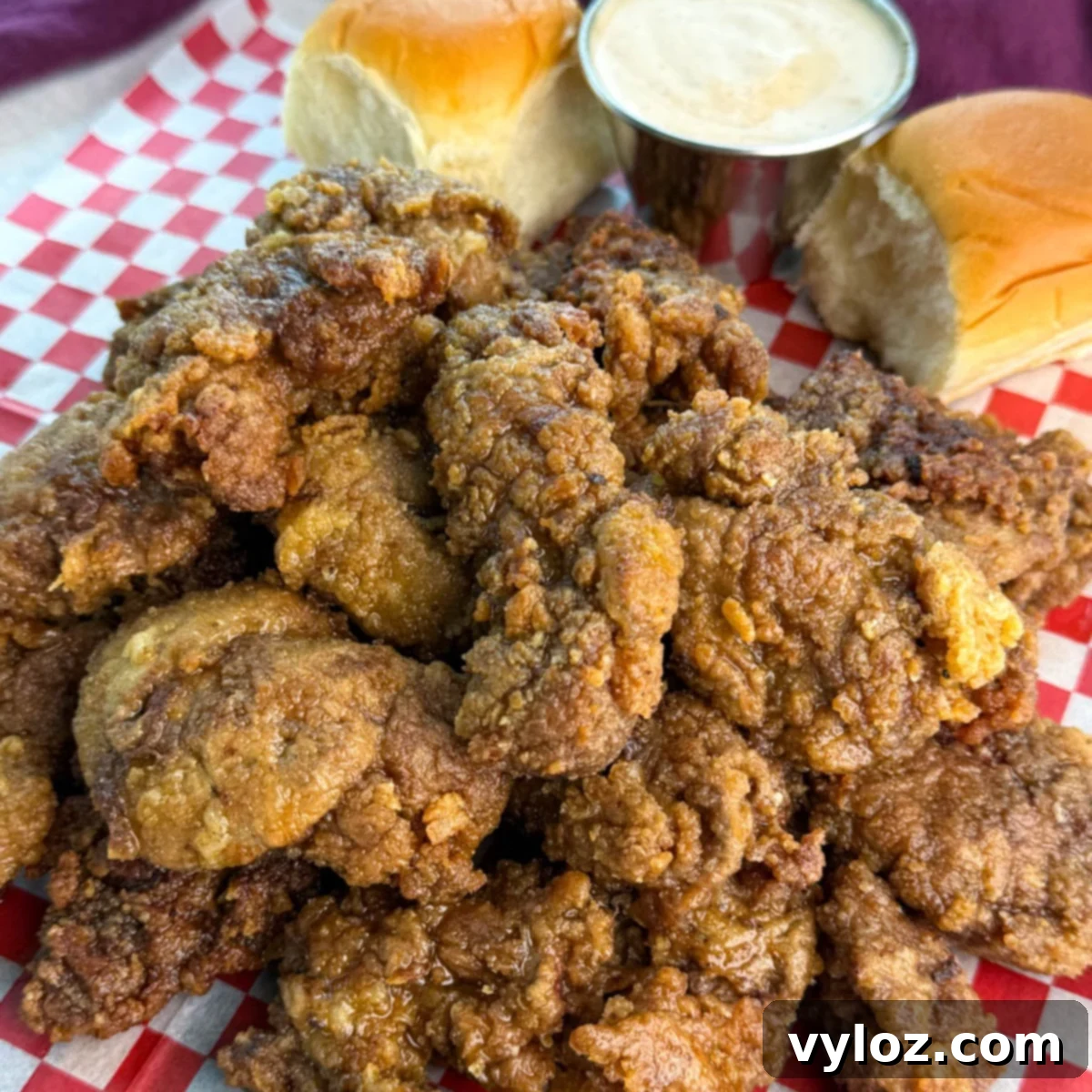 Crispy Fried Chicken Livers 2 A generous serving of crispy fried chicken livers piled high on a tray lined with checkered paper, with rolls and sauce on the side.