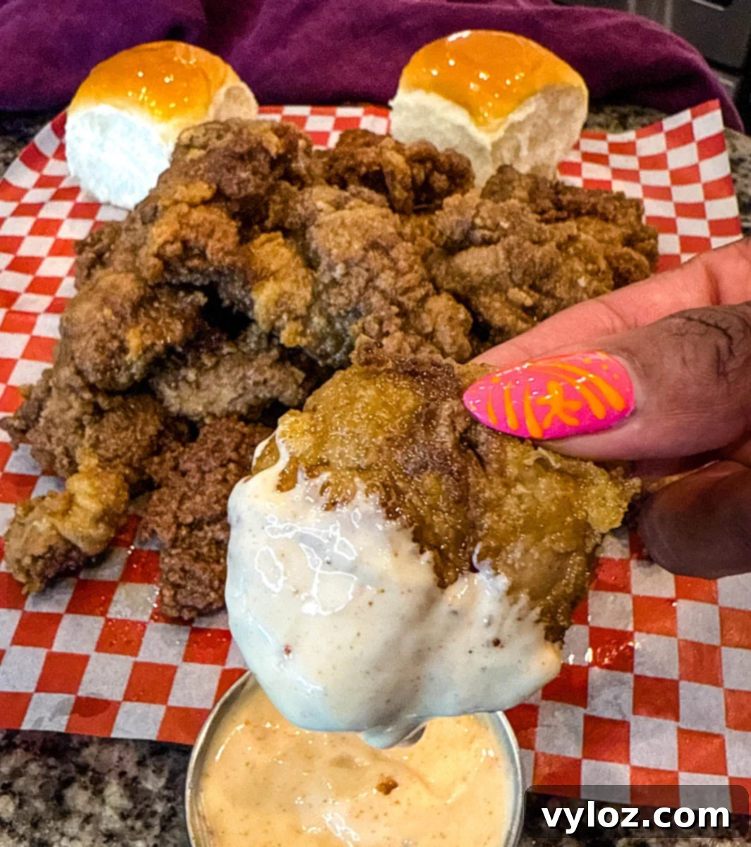 Crispy Fried Chicken Livers 11 A hand holding a crispy fried chicken liver over a small metal cup of dipping sauce, with a pile of fried livers in the background.